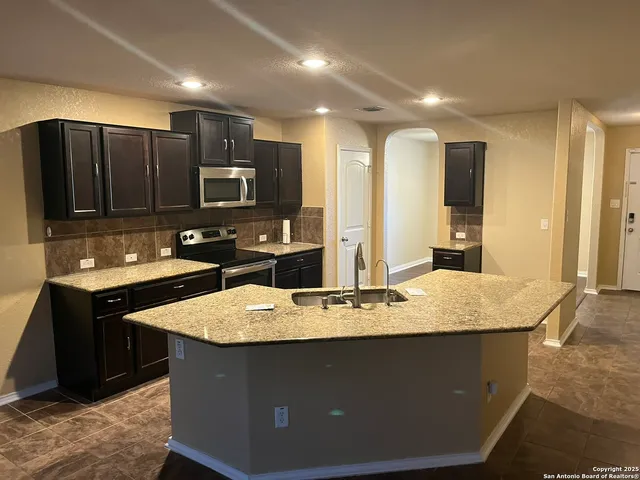 a kitchen with kitchen island granite countertop a sink stove and refrigerator
