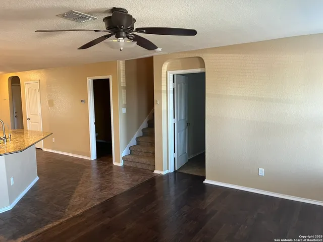 a view of an empty room with wooden floor and a ceiling fan