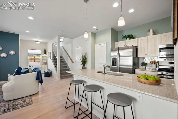 a room with stainless steel appliances kitchen island granite countertop a dining table chairs and couches with wooden floor
