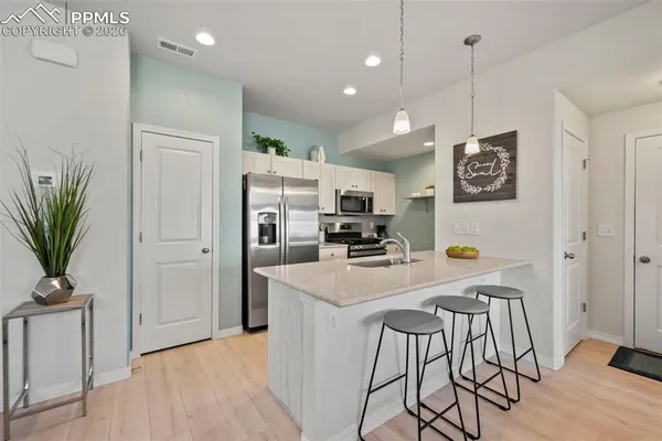 a kitchen with stainless steel appliances a stove a refrigerator a sink a dining table and chairs with wooden floor