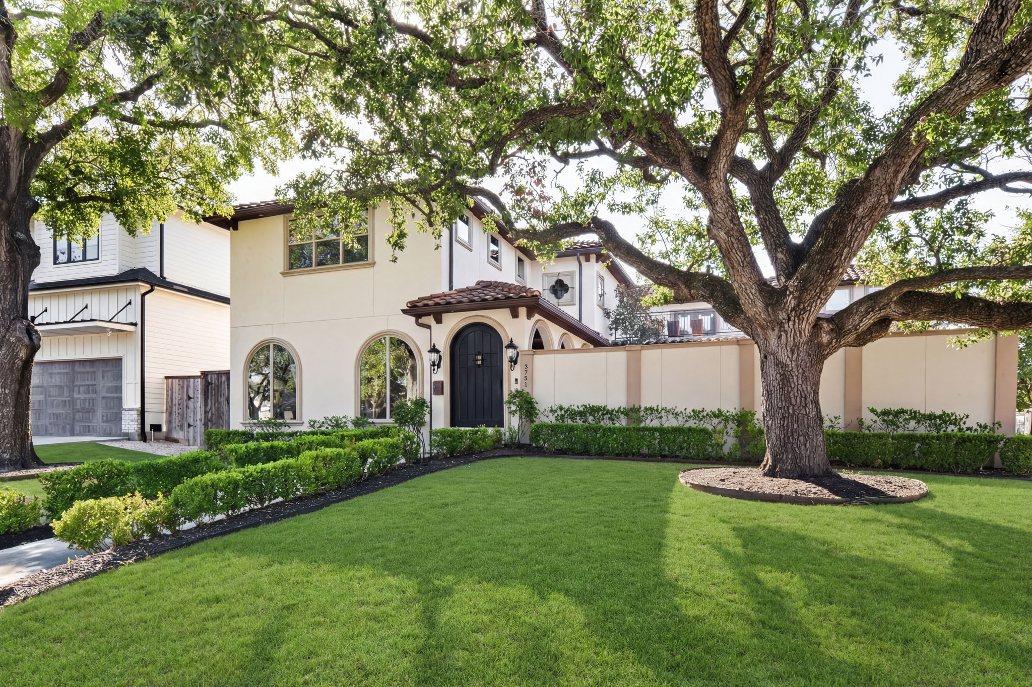 A beautiful Mediterranean-style exterior set on a premier corner lot, framed by mature, sprawling oak trees and lush landscaping that provide exceptional privacy, with arched windows, smooth stucco, and a gated courtyard creating a serene and secluded street presence.