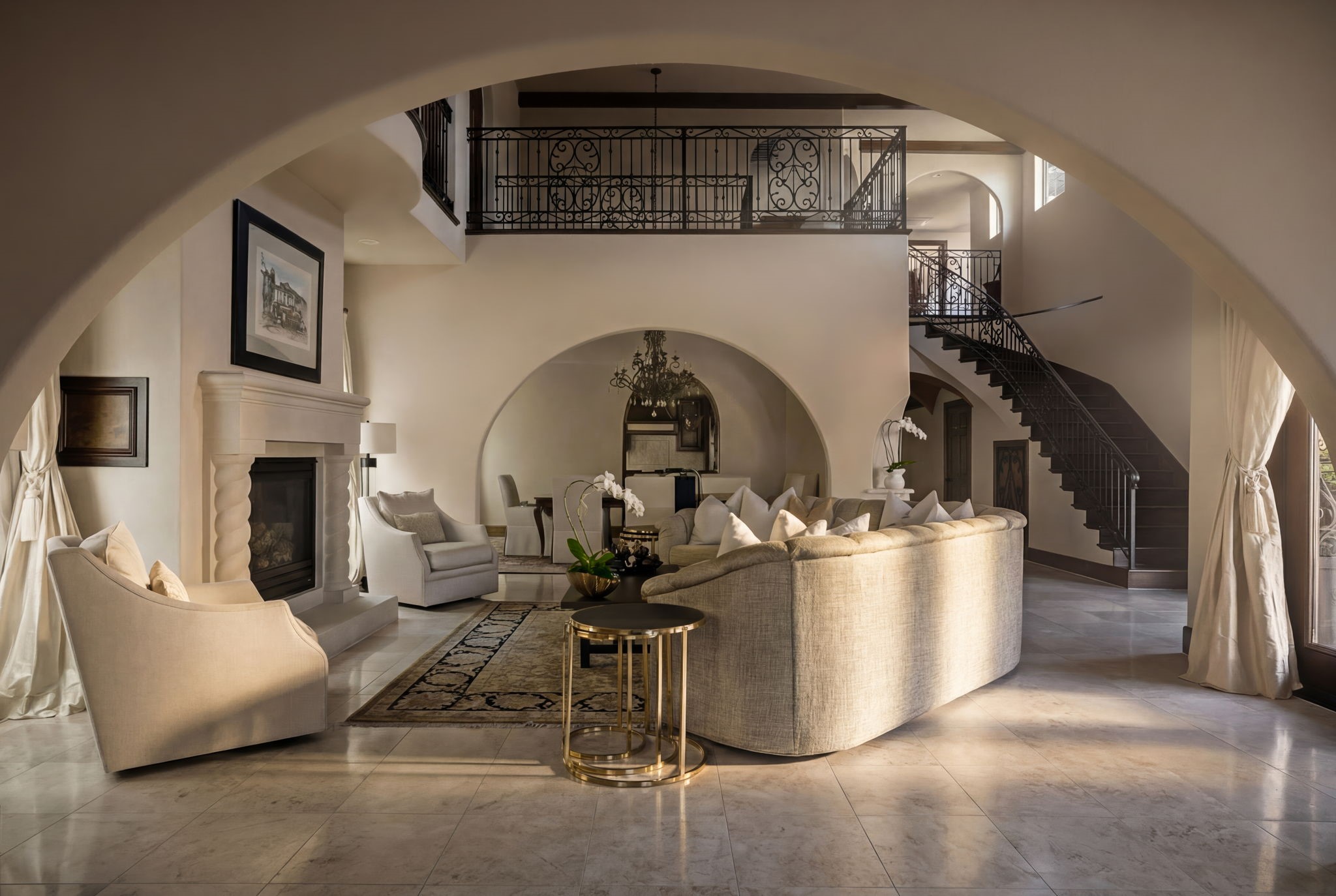 3751 Aberdeen Way Houston, TX 77025 - Photo 6 of 39 An elegant, light-filled living space framed by sweeping architectural arches, layered with a dramatic second-level gallery and ornate iron railings, while a sculptural staircase and classic fireplace create a refined sense of symmetry and grand scale.