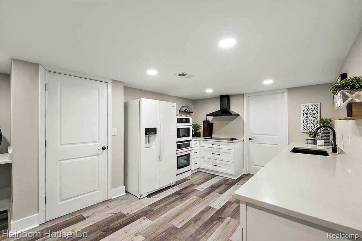 49001 Hanford Road Canton, MI 48187 - Photo 57 of 98 Modern kitchen featuring wood-finish flooring, white cabinetry, integrated stainless steel appliances, a black range hood, and solid surface countertops