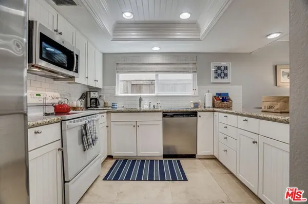 a kitchen with granite countertop a sink stainless steel appliances and white cabinets