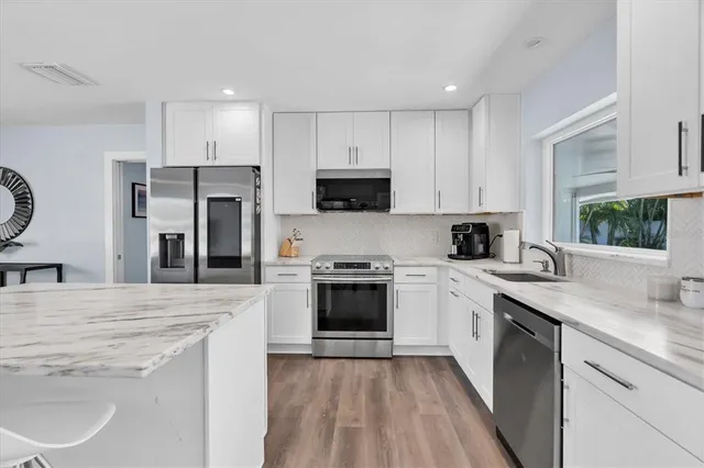 a kitchen with kitchen island a stove a microwave a sink a refrigerator and white cabinets