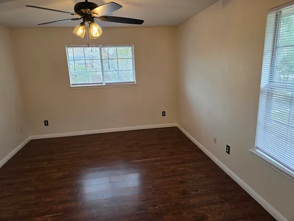 an empty room with wooden floor fan and windows