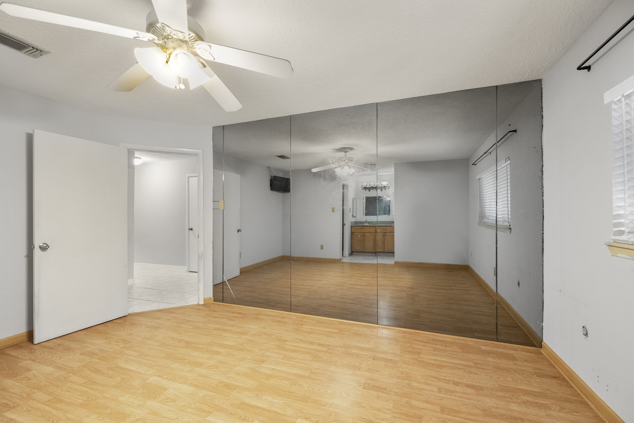 23826 Lestergate Drive Spring, TX 77373 - Photo 20 of 45 Turning back across the primary bedroom, the mirrored accent wall reflects light through the space and gives you another look at the ensuite bath beyond. The window along the right brings in additional natural light, while the ceiling fan and simple suite layout keep the room feeling comfortable and connected.