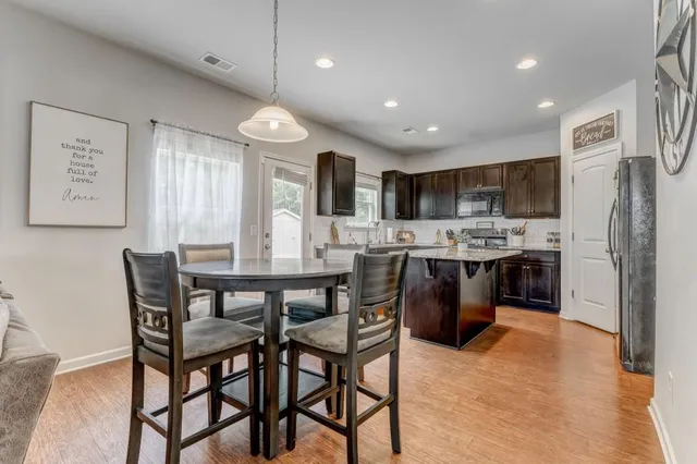 a kitchen with stainless steel appliances kitchen island granite countertop a dining table chairs and a refrigerator