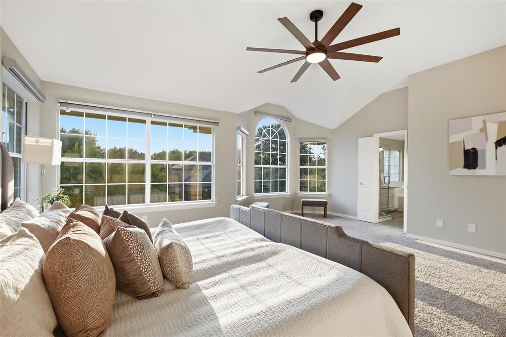 3903 Rive Lane Addison, TX 75001 - Photo 19 of 40 Sunlight pours through the arched and gridded windows of the primary bedroom, highlighting the vaulted ceiling and the generous proportions of this rear-facing retreat. The entry to the primary bathroom is visible in the background, completing the private suite layout.