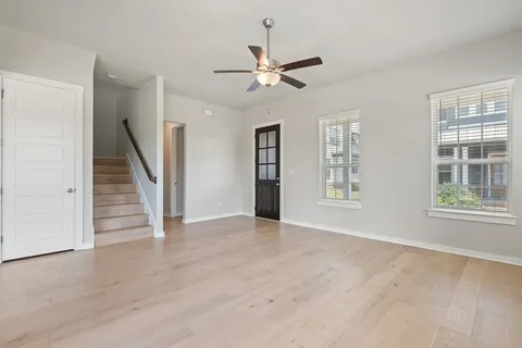 a view of an empty room with wooden floor ceiling fan and window