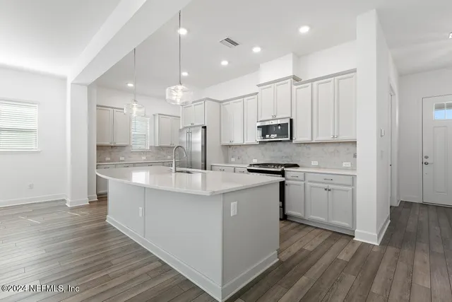 a view of an empty room with wooden floor and a kitchen