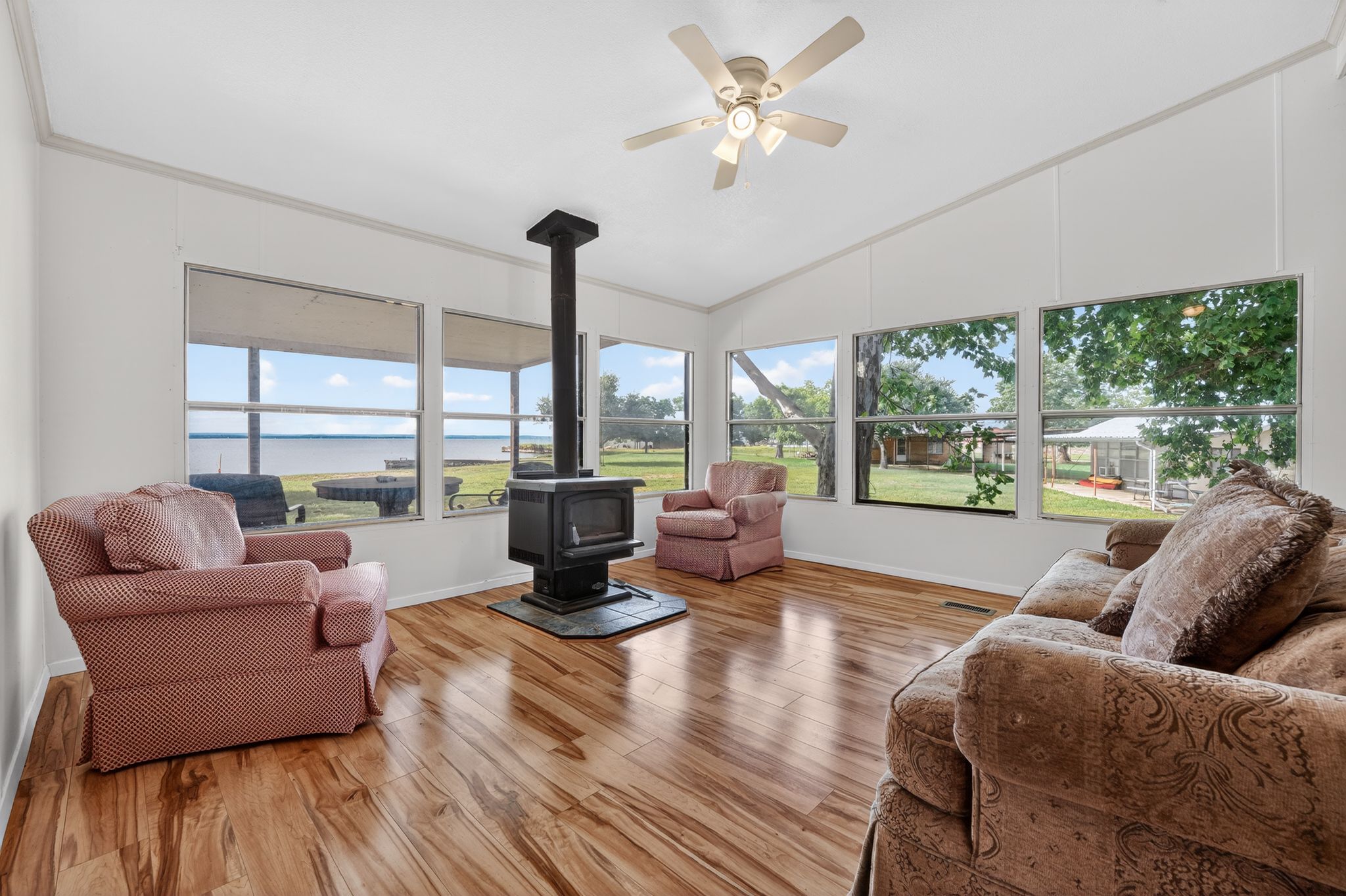 1192 County Road 225 Bluffton, TX 78607 - Photo 26 of 38 Spacious living area featuring expansive windows, wood-finish flooring, and a freestanding wood-burning stove on a stone hearth
