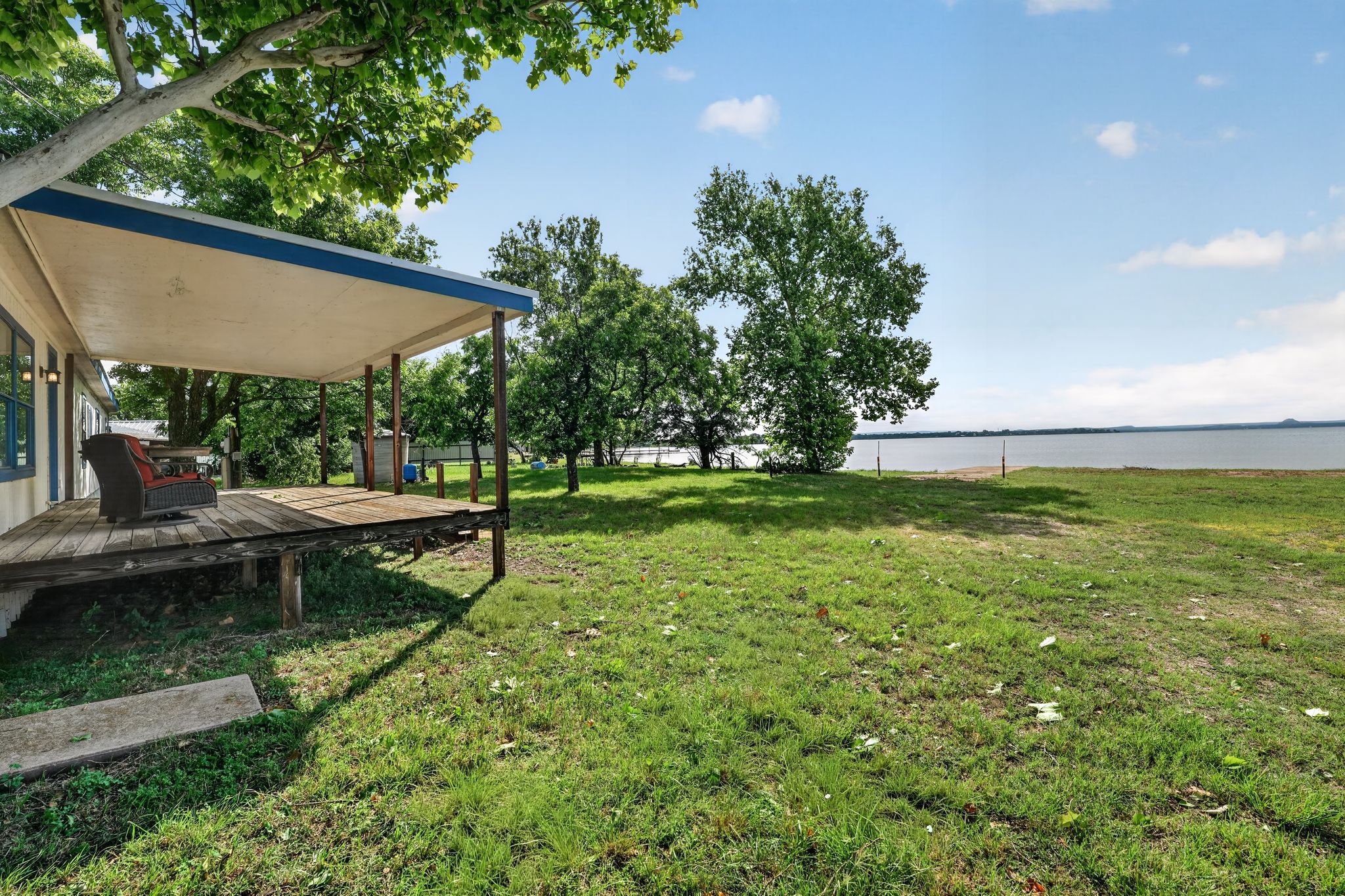 1192 County Road 225 Bluffton, TX 78607 - Photo 33 of 38 Expansive waterfront property featuring a covered porch with a wood-finish deck, mature shade trees, and a substantial grassy area extending to the water's edge