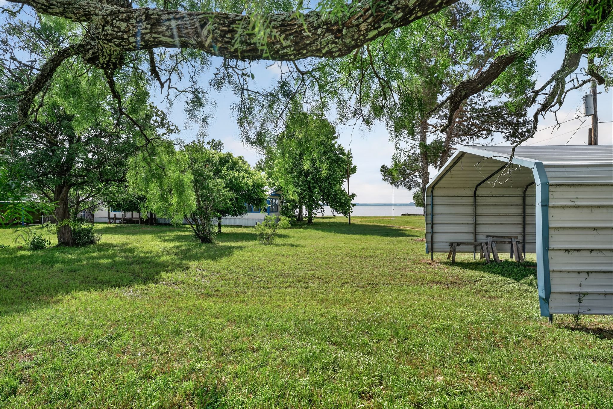 1192 County Road 225 Bluffton, TX 78607 - Photo 36 of 38 Expansive green lawn with mature trees and a metal carport structure