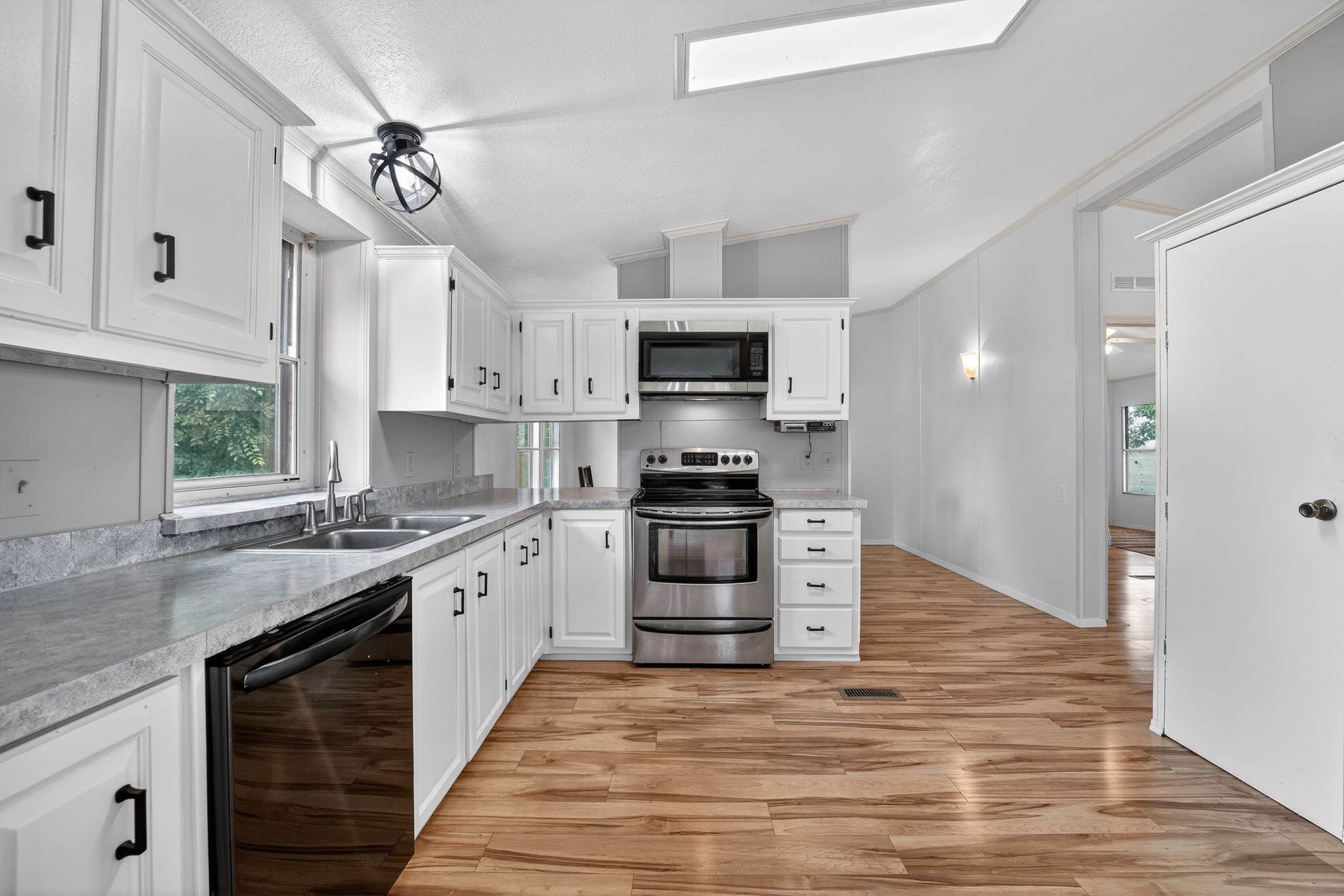 1192 County Road 225 Bluffton, TX 78607 - Photo 8 of 38 Kitchen featuring white cabinetry with black hardware, stainless steel appliances, a dual basin sink with a gooseneck faucet, light grey countertops, and wood-finish flooring
