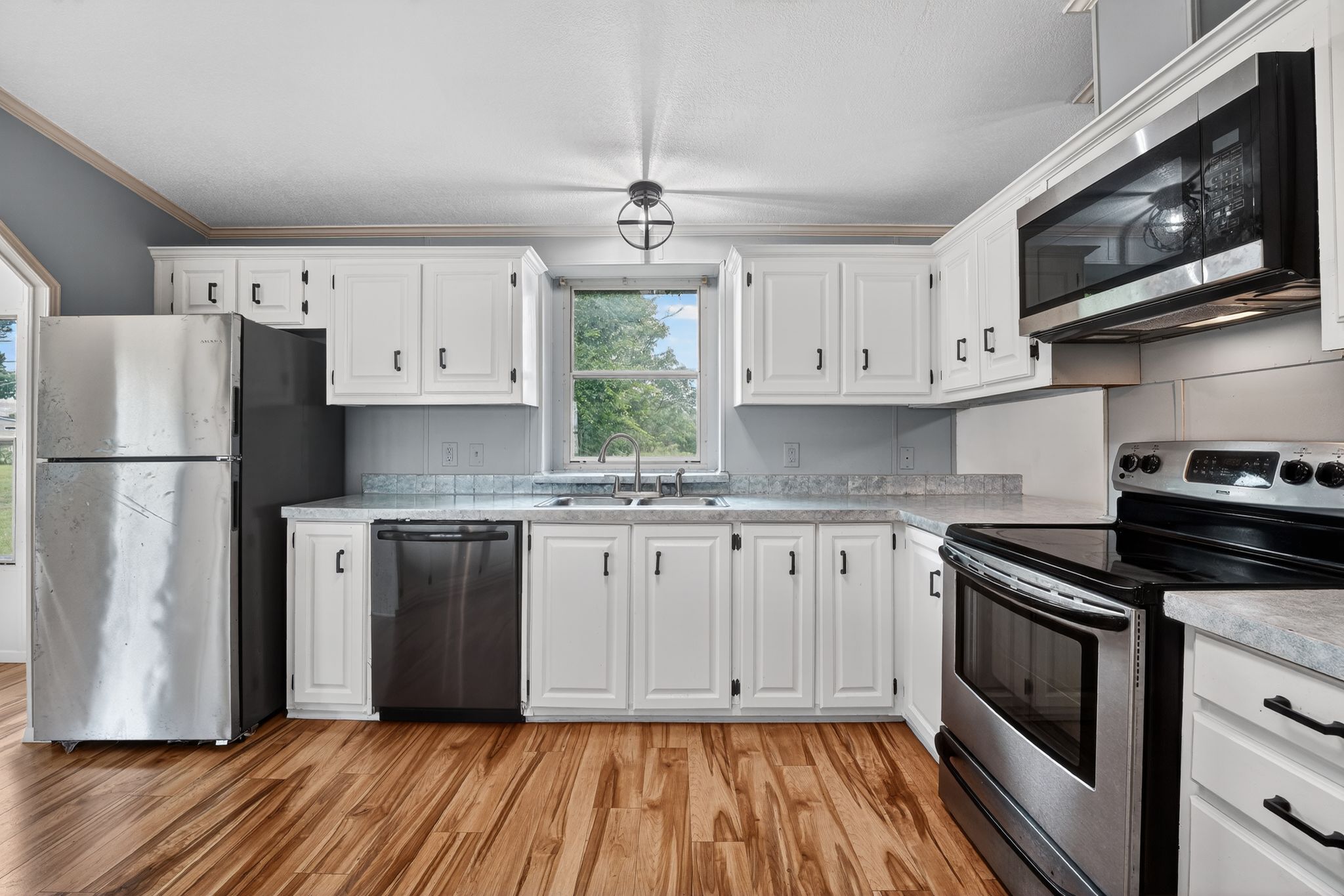1192 County Road 225 Bluffton, TX 78607 - Photo 10 of 38 Kitchen featuring white cabinetry with dark hardware, stainless steel appliances, wood-finish flooring, and a double basin sink beneath a window