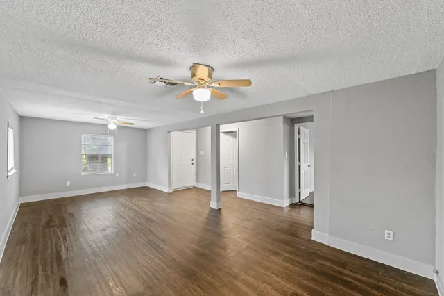 a view of an empty room with wooden floor and a ceiling fan