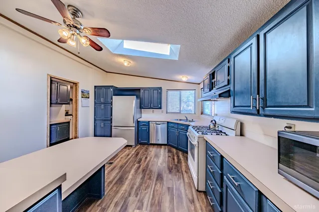 a kitchen with stainless steel appliances granite countertop a refrigerator a sink dishwasher a stove and a dining table with wooden floor