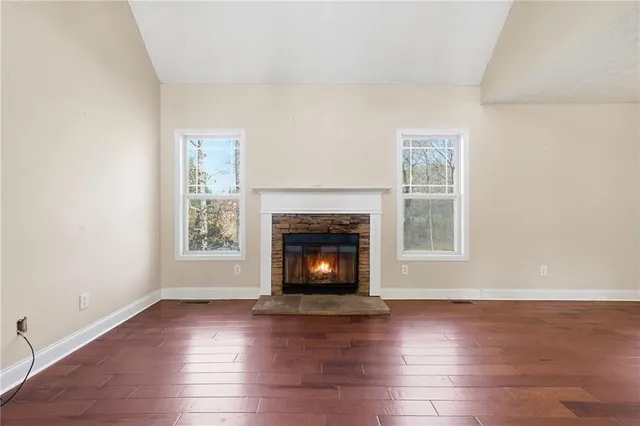an empty room with wooden floor fireplace and windows