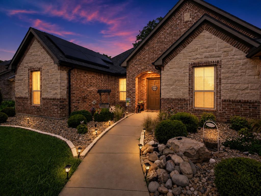 701 West Lamberth Road Sherman, TX 75092 - Photo 1 of 37 Brick and stone facade featuring a gabled roofline with solar panels, a concrete walkway with integrated pathway lighting, and a landscaped front yard with decorative rocks and shrubs