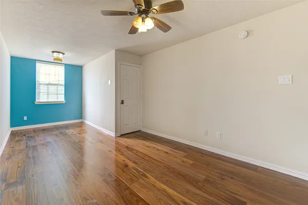 an empty room with wooden floor fan and windows