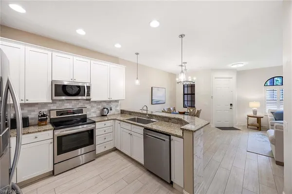 a kitchen with stainless steel appliances granite countertop a stove top oven a sink dishwasher a refrigerator and white cabinets with wooden floor