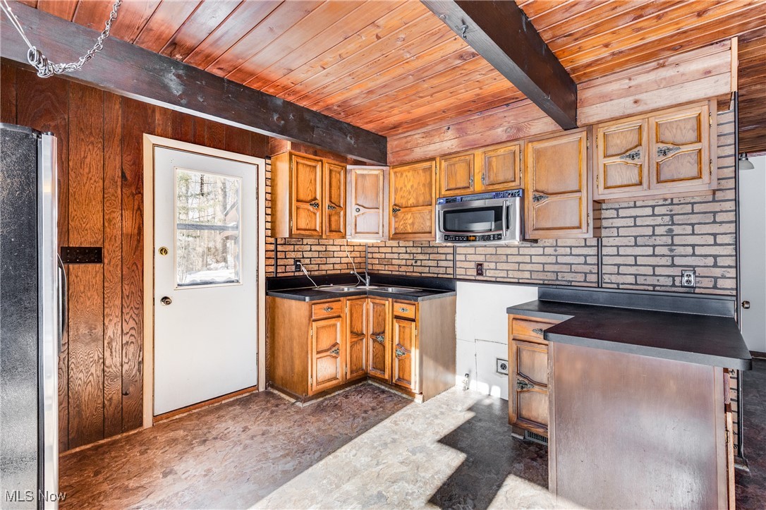 Kitchen with a wood ceiling with exposed beams, wood finish cabinets, dark countertops, and stainless steel appliances