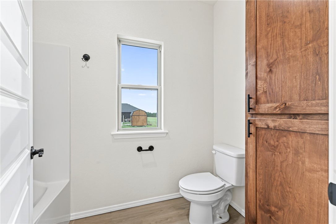 6138 New Hope Road Hackett, AR 72937 - Photo 23 of 56 White paneled door, wood-finish flooring, white toilet, and built-in wood cabinetry with black hardware
