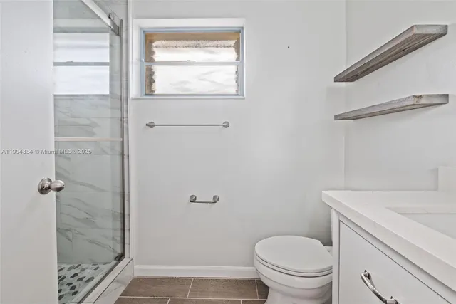 a bathroom with a granite countertop toilet a sink a shower and a window