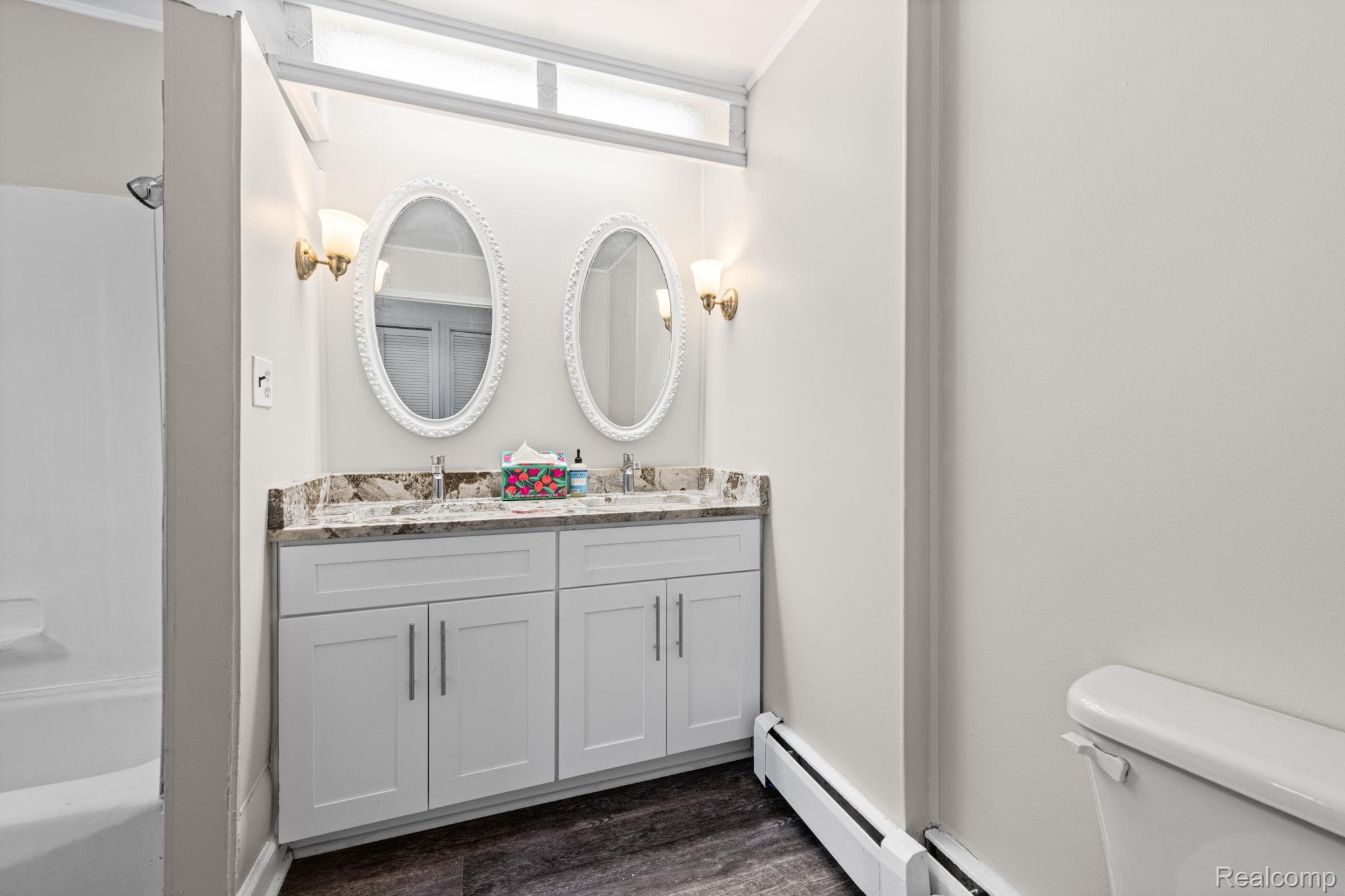 7993 Church Road Grosse Ile, MI 48138 - Photo 16 of 37 Bathroom featuring a dual vanity with a patterned countertop, two oval mirrors with ornate white frames, and wall-mounted sconce lighting