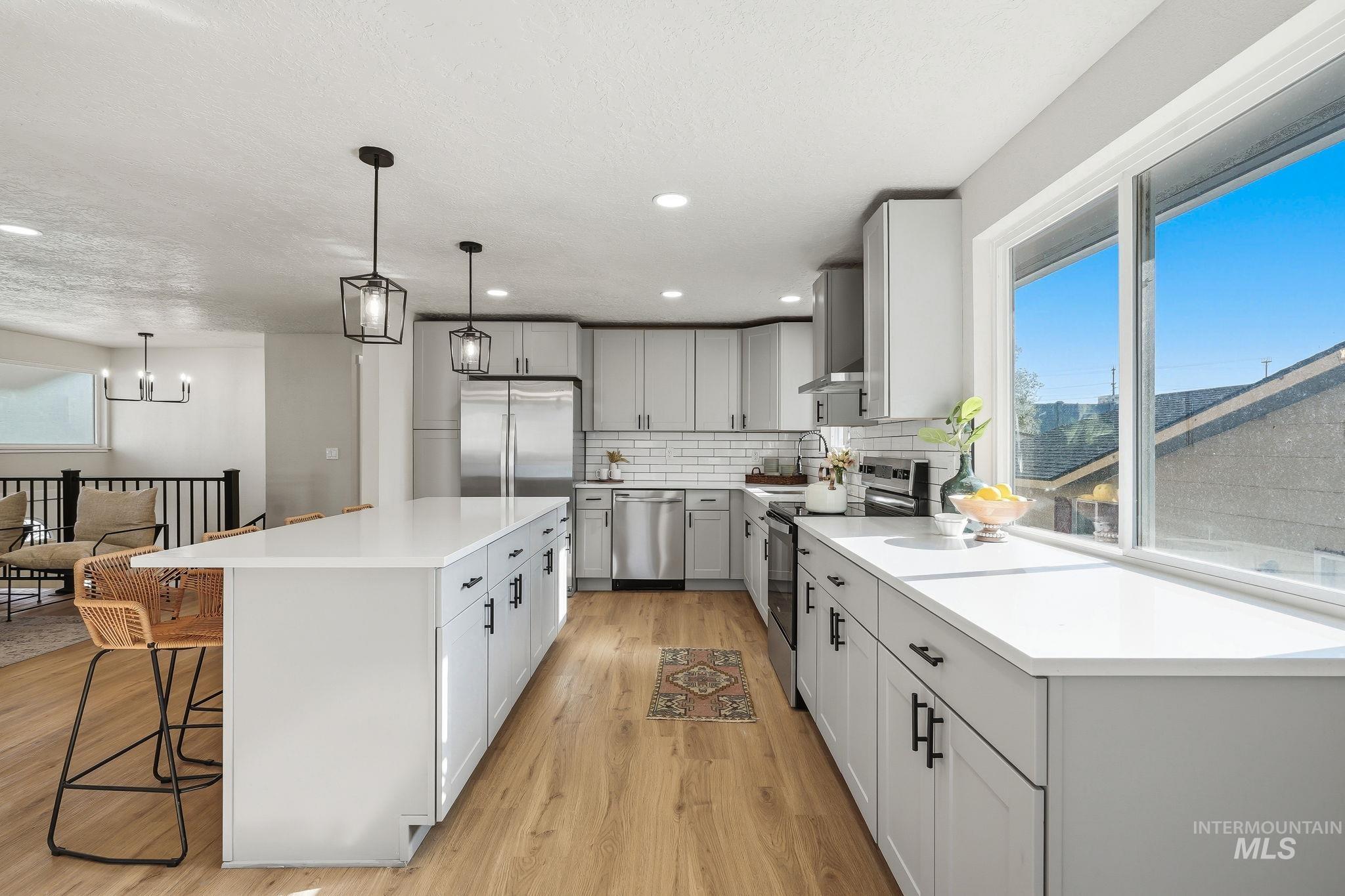 1990 Panama Street Boise, ID 83705 - Photo 23 of 50 Modern kitchen featuring an expansive center island with pendant lighting, light wood-finish flooring, white subway tile backsplash, stainless steel appliances, and a large window
