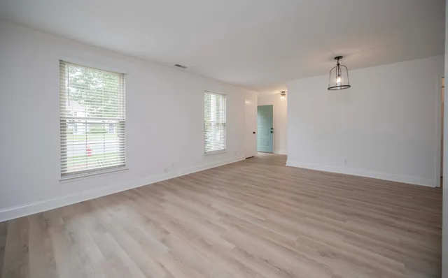 an empty room with wooden floor ceiling fan and windows