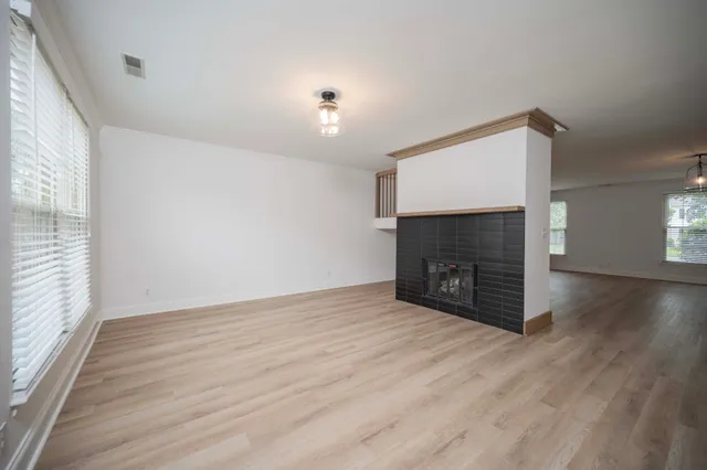 a view of an empty room with wooden floor fireplace and a window
