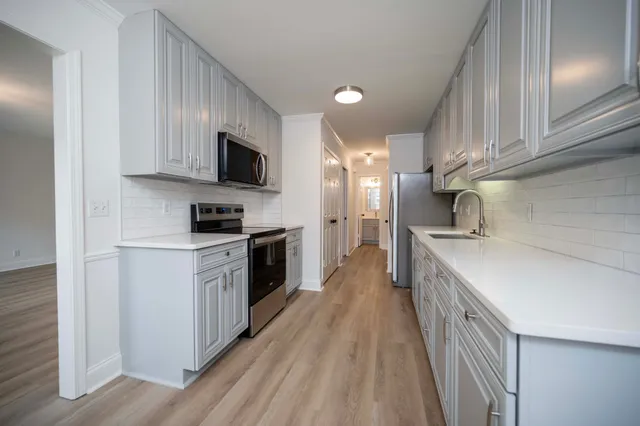 a kitchen with stainless steel appliances a stove top oven a sink a refrigerator white cabinets and wooden floor