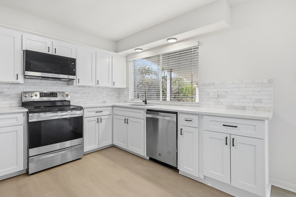 2204 Toro Canyon Road Austin, TX 78746 - Photo 12 of 26 Kitchen with stainless steel appliances, white cabinetry, light wood finished floors, light stone counters, and backsplash