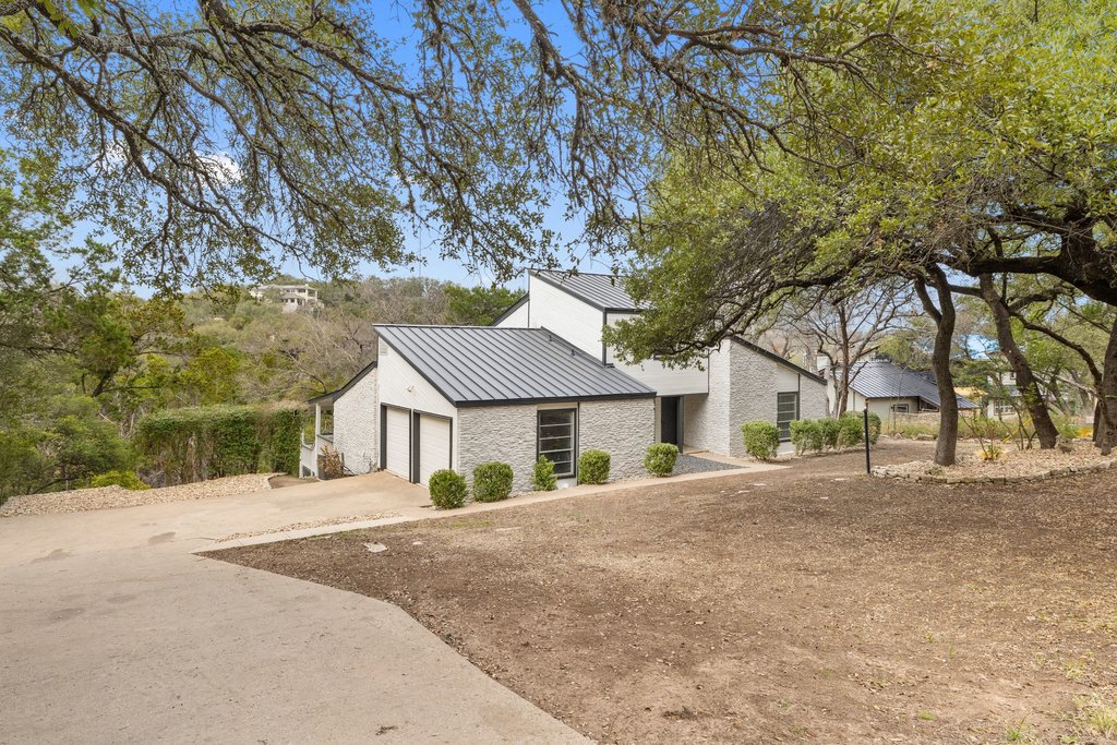2204 Toro Canyon Road Austin, TX 78746 - Photo 4 of 26 View of home's exterior with a standing seam roof, driveway, an attached garage, and brick siding