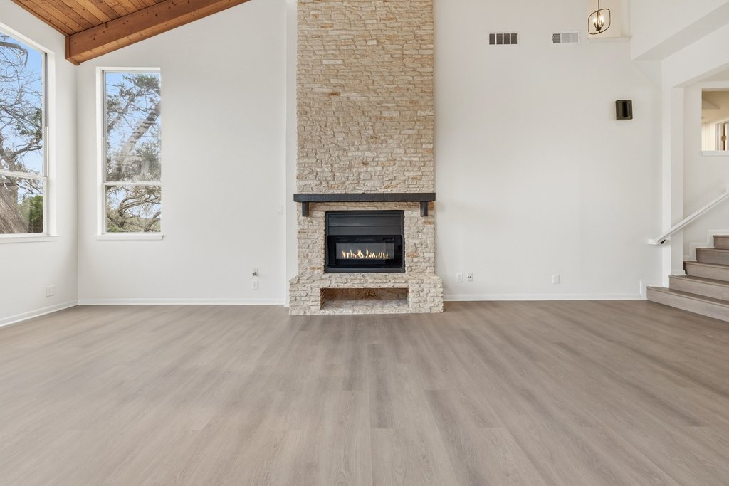 2204 Toro Canyon Road Austin, TX 78746 - Photo 7 of 26 Unfurnished living room featuring light wood finished floors, vaulted ceiling, and a stone fireplace