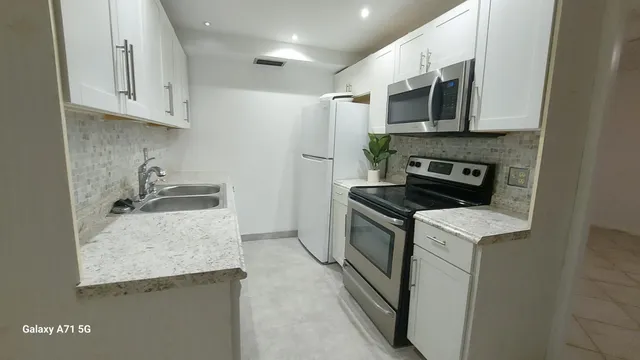 a kitchen with stainless steel appliances granite countertop a stove top oven a sink a refrigerator and white cabinets