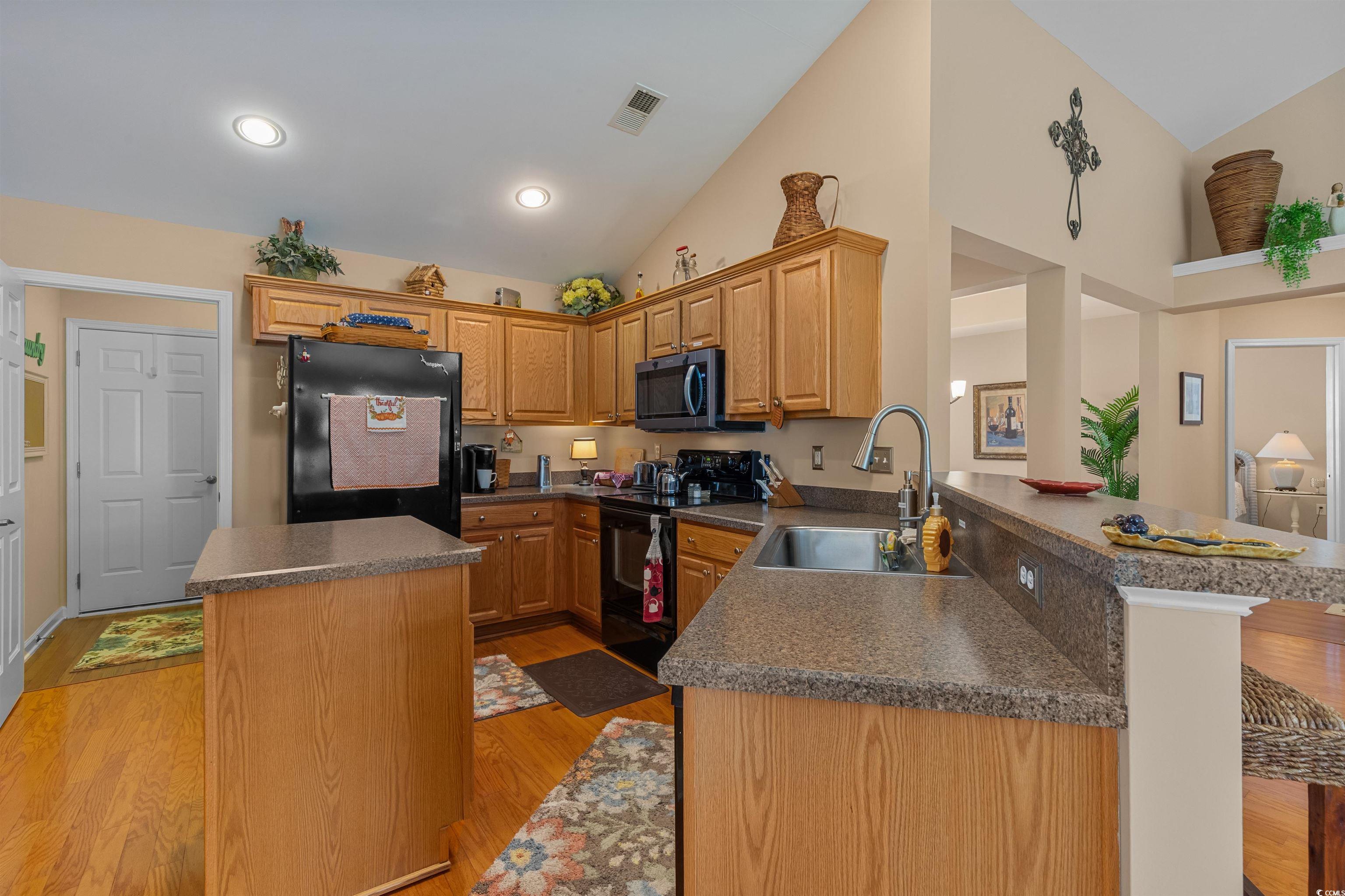 3505 Arrowhead Boulevard Myrtle Beach, SC 29579 - Photo 10 of 40 Kitchen with black appliances, a kitchen island, light wood-style flooring, dark countertops, and a peninsula