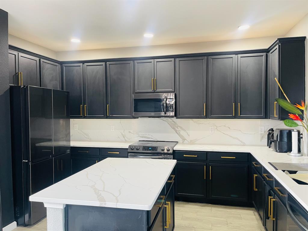 516 Angela Lane Euless, TX 76039 - Photo 11 of 39 Kitchen featuring light stone counters, black appliances, a center island, light wood-style floors, and decorative backsplash