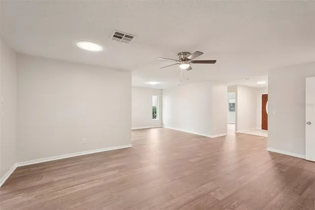 an empty room with wooden floor chandelier fan and windows