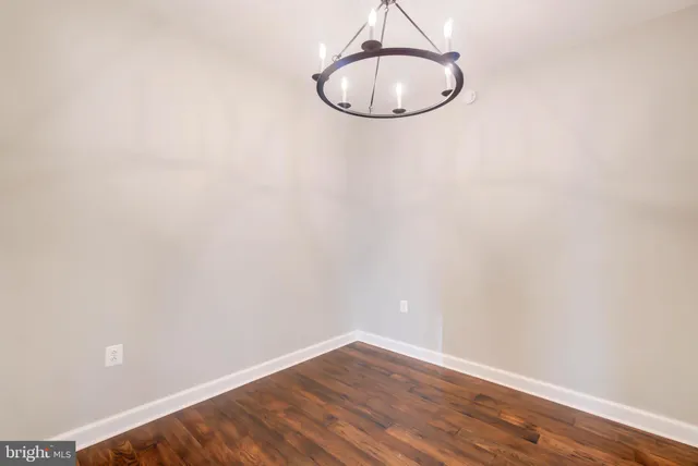 an empty room with a chandelier fan and wooden floor