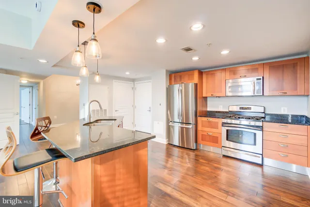 a kitchen with stainless steel appliances granite countertop a sink a stove a refrigerator and island with wooden floor