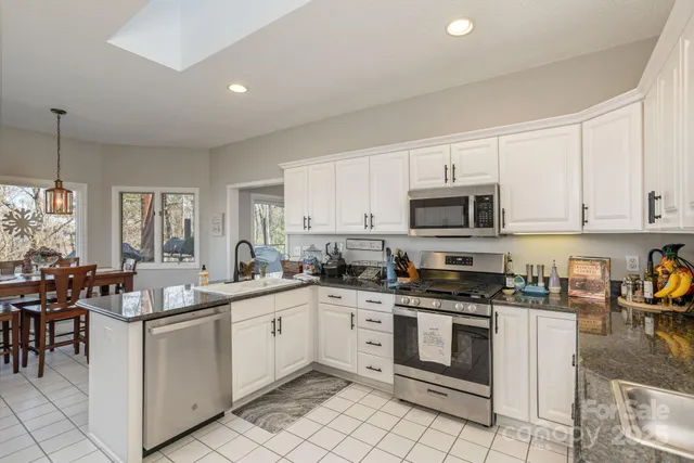 a kitchen with stainless steel appliances granite countertop a stove top oven a sink a dining table and chairs with white cabinets