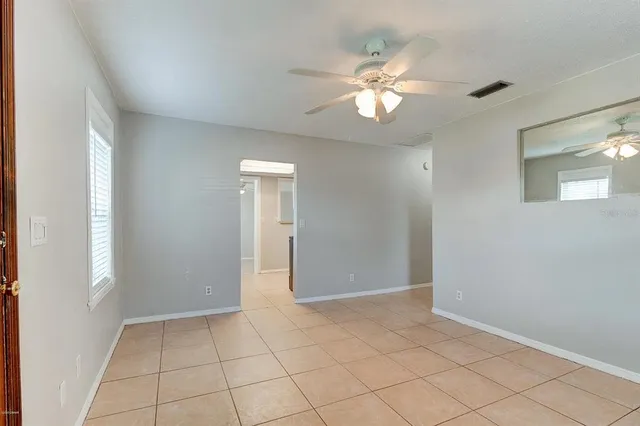 a view of an empty room with window and chandelier fan