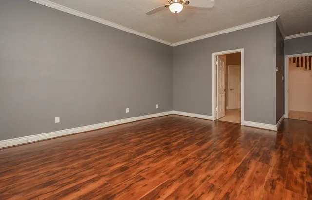 a view of an empty room with wooden floor and a ceiling fan