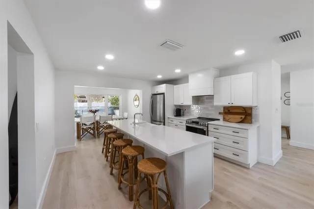 a kitchen with stainless steel appliances kitchen island granite countertop a stove top oven a sink a refrigerator with white cabinets and wooden floor