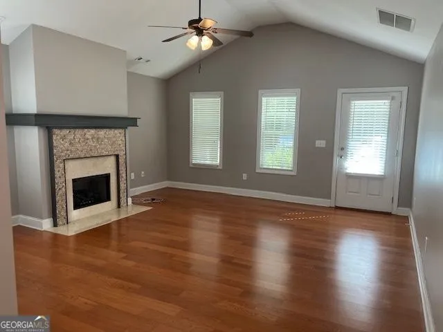 a view of an empty room with wooden floor fireplace and a window
