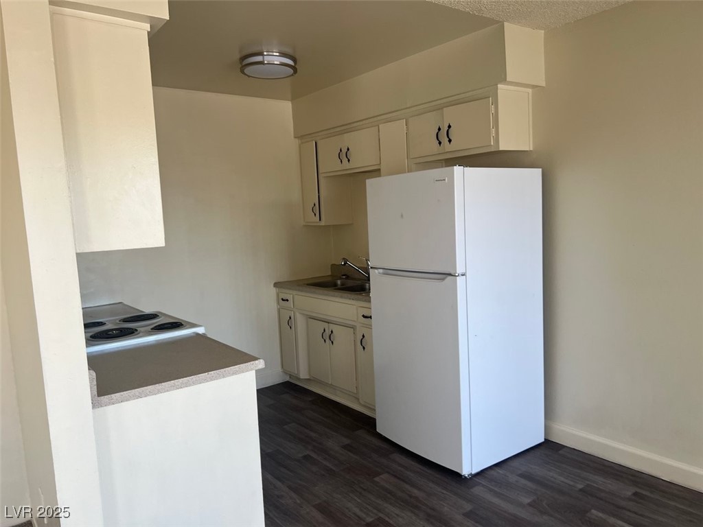 1388 East Desert Inn Road, Unit 1 Las Vegas, NV 89169 - Photo 3 of 17 Kitchen featuring white appliances, a sink, dark wood-style floors, white cabinets, and baseboards