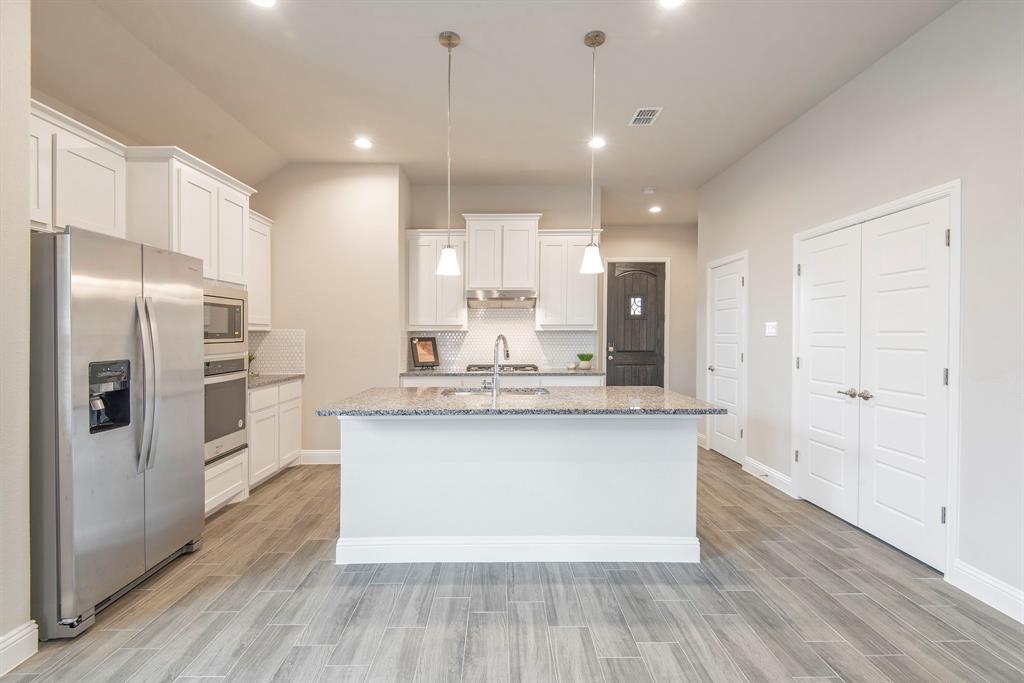 2301 Ruff Road Denton, TX 76205 - Photo 7 of 23 Kitchen featuring a central island with a sink, pendant lighting, stainless steel appliances, white cabinetry, and wood-look tile flooring